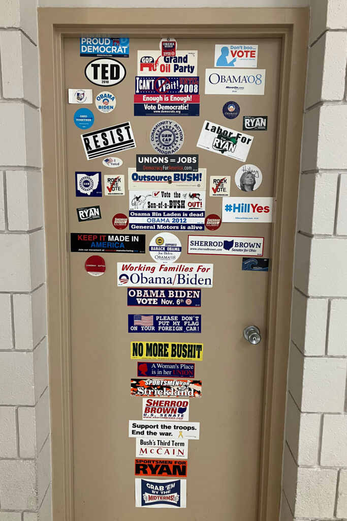 Bumper stickers adorn a door at the UAW hall in Lordstown, Ohio. The union is active in politics, while also saying that politics should not play a role in someone's choice of whether to drive an EV or not. Credit: Dan Gearino/Inside Climate News